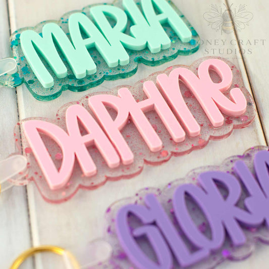 Close-up of custom glitter acrylic name tags showing layered 3D names and colorful confetti backgrounds.