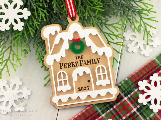 Custom Gingerbread House Christmas ornament engraved with “The Perez Family 2025,” featuring white icing details and a red-striped ribbon from Honey Craft Studios.