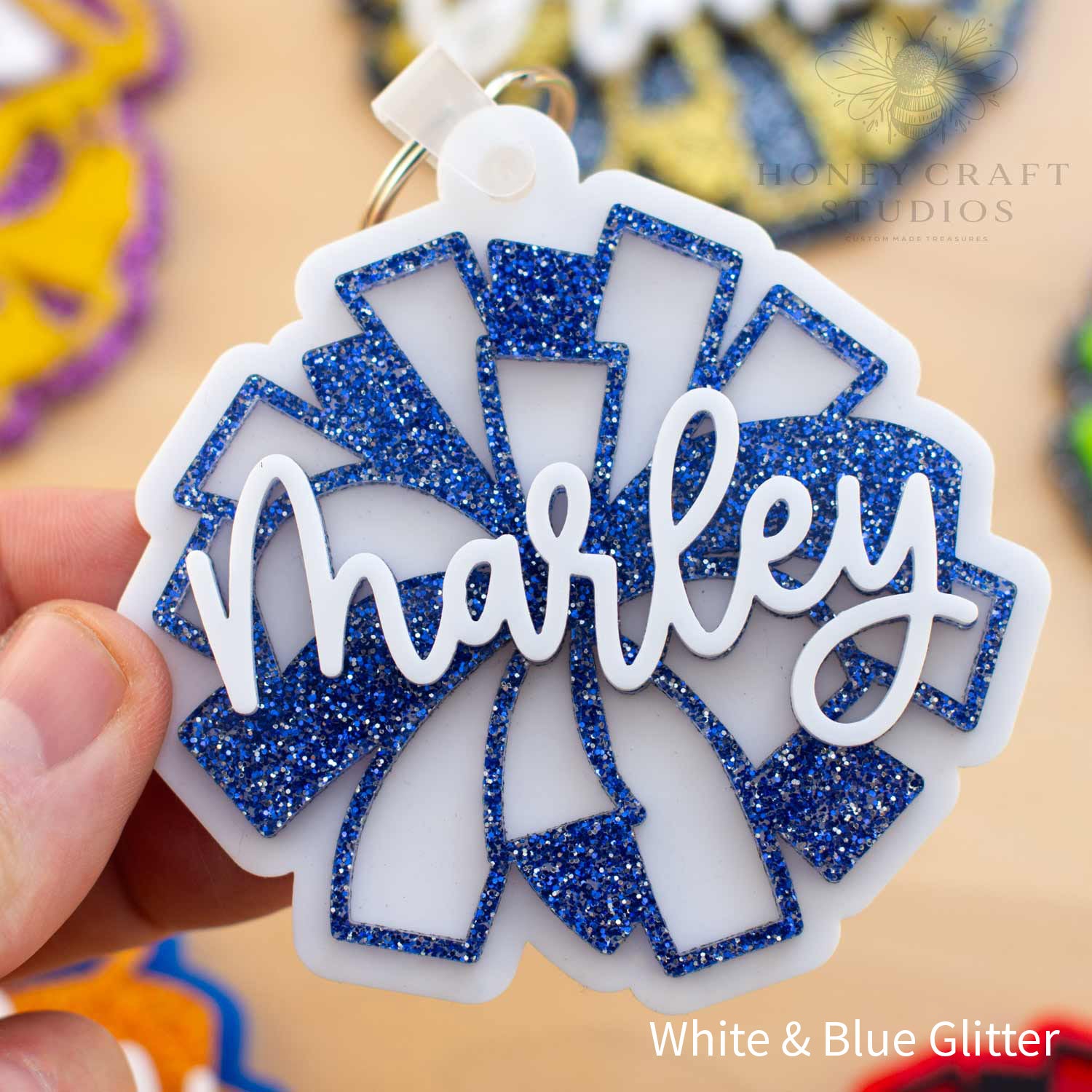 Custom cheer pom-pom bag tag in white acrylic with blue glitter pom-pom accents, personalized with the name “Marley” in raised white script lettering.