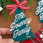 Personalized Christmas tree ornament with 'The Downey Family 2025' text on a wooden surface.