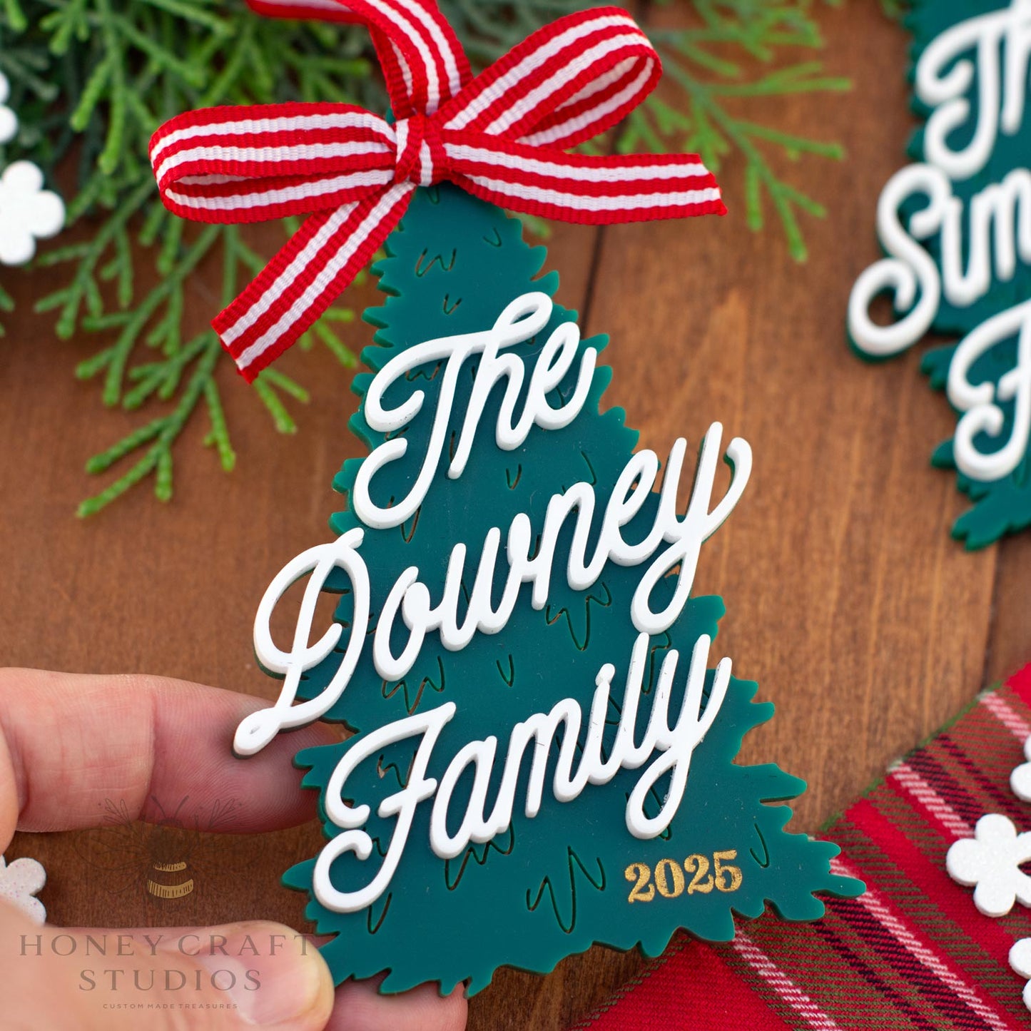 Personalized Christmas tree ornament with 'The Downey Family 2025' text on a wooden surface.