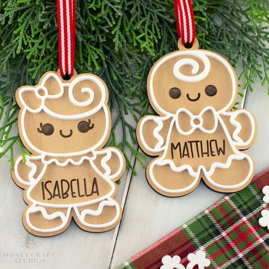 Two wooden gingerbread cookie ornaments with names 'Isabella' and 'Matthew' hanging on a branch.