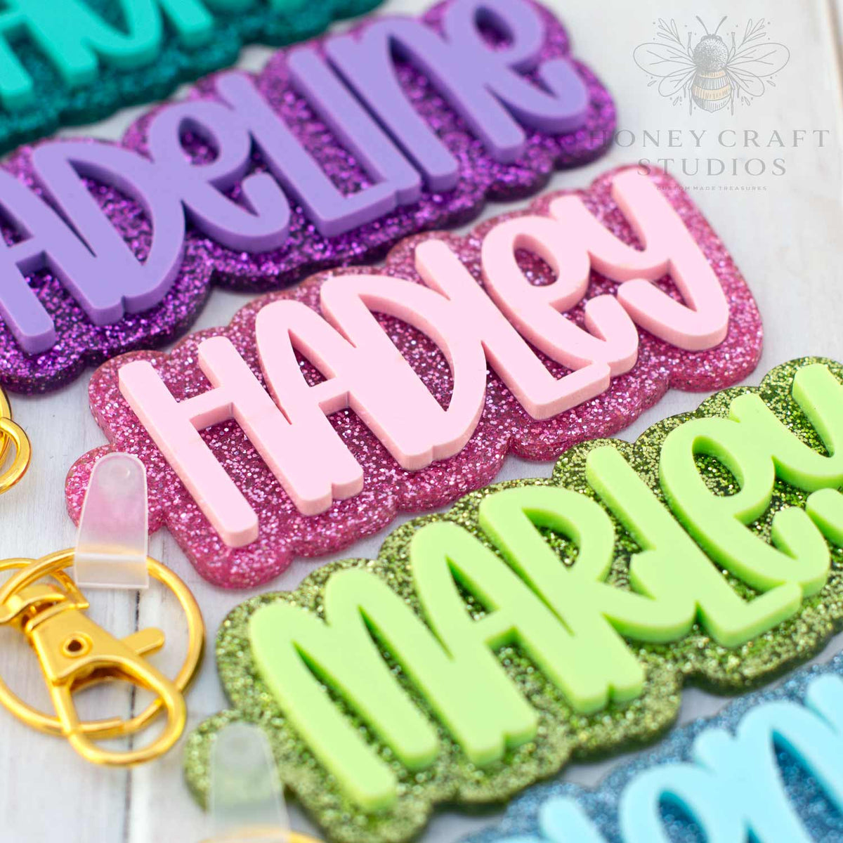 Colorful custom name keychains made of layered glitter acrylic with bold names, perfect for backpacks or cheer bags.