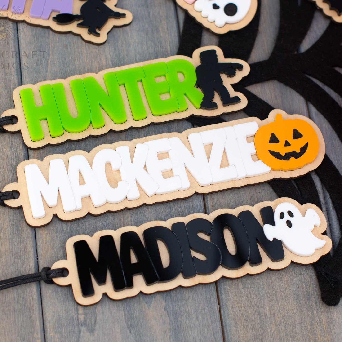 Personalized wooden Halloween name signs spelling HUNTER, MACKENZIE, and MADISON, each with a spooky character silhouette or ghost detail, displayed on a dark wood background.