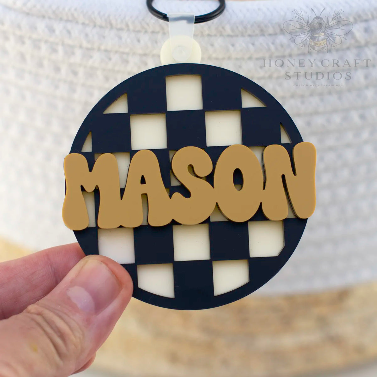 Black checkered circle name tag with bold mustard yellow text, ideal for custom backpack accessories.