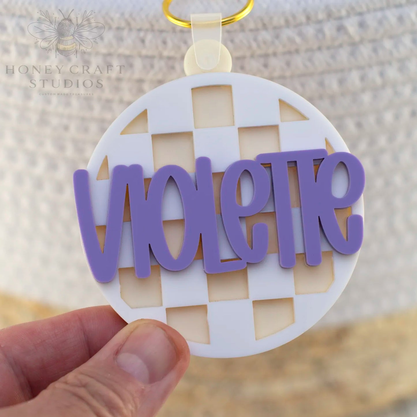 White acrylic checkered name tag featuring layered purple custom name, made for school kids and bags.