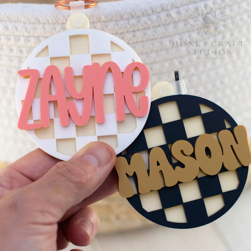 Custom acrylic checkered circle name tags for kids, shown in white with pink Zayne and black with mustard Mason text.