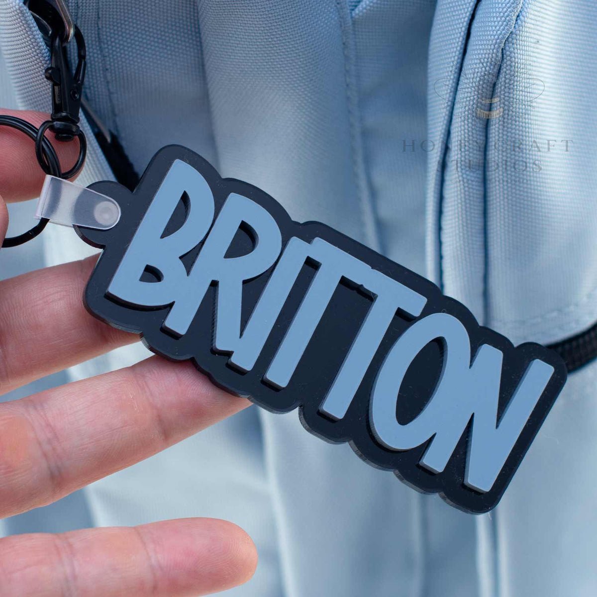 Personalized acrylic name keychain in Slate Blue with black backing, designed for labeling boys’ backpacks or school bags.