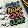 Custom acrylic name keychains in bold colors (Slate Blue, Mustard, Terracotta, and Fern Green), personalized with boys’ names, ideal for backpacks, school bags, and gifts.