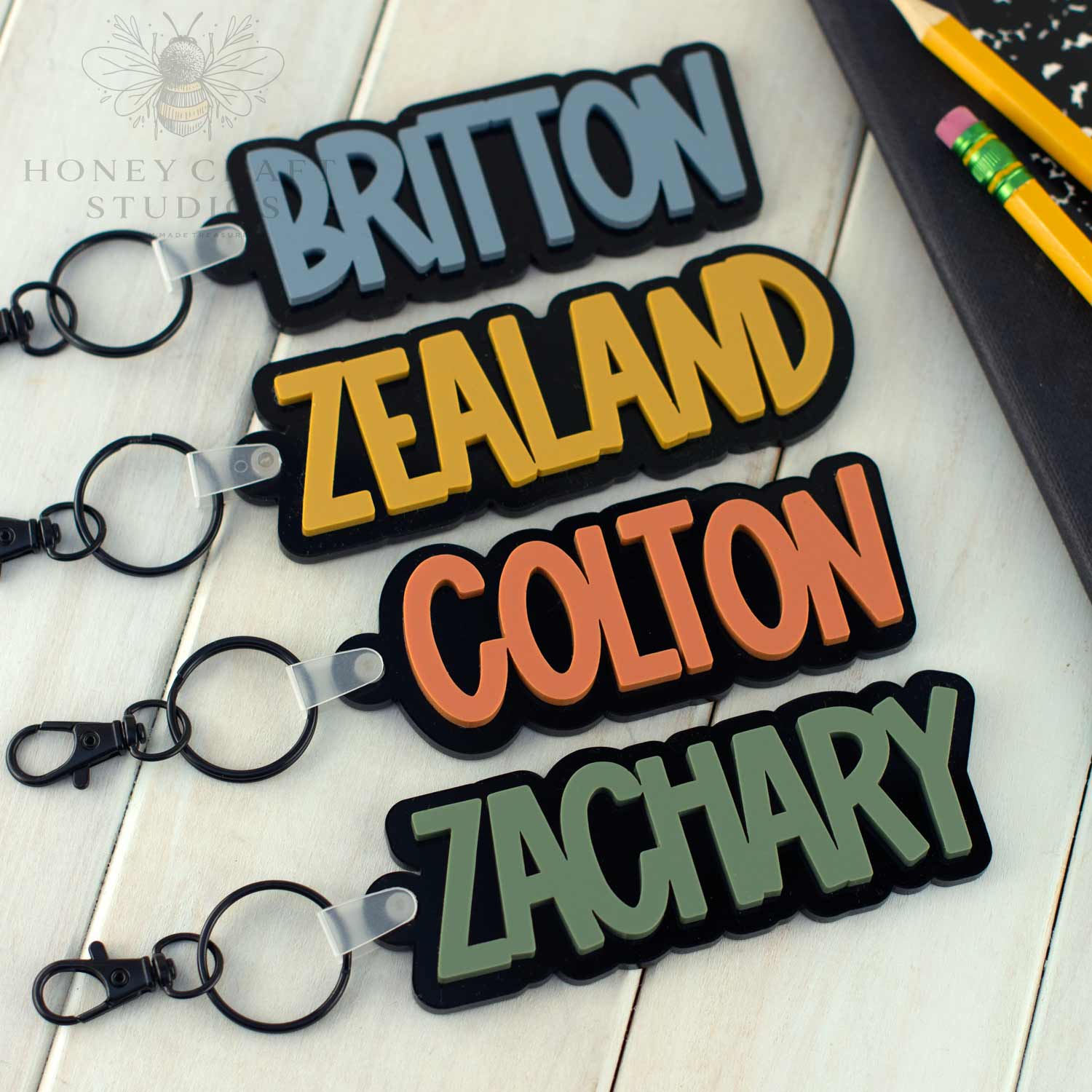 Custom acrylic name keychains in bold colors (Slate Blue, Mustard, Terracotta, and Fern Green), personalized with boys’ names, ideal for backpacks, school bags, and gifts.