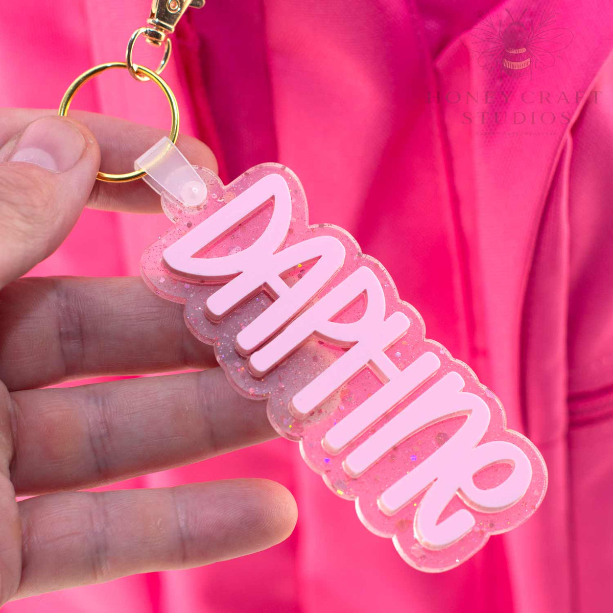 Personalized pink glitter name tag reading “Daphne” attached to a child’s backpack zipper.