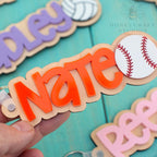 Custom baseball name keychain with orange acrylic lettering and engraved wood base, featuring baseball icon