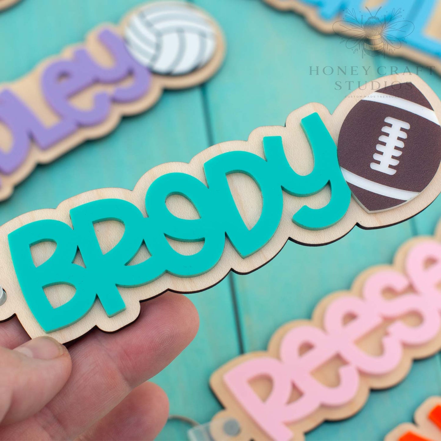 Custom football name keychain with teal acrylic lettering on wood base and engraved football icon