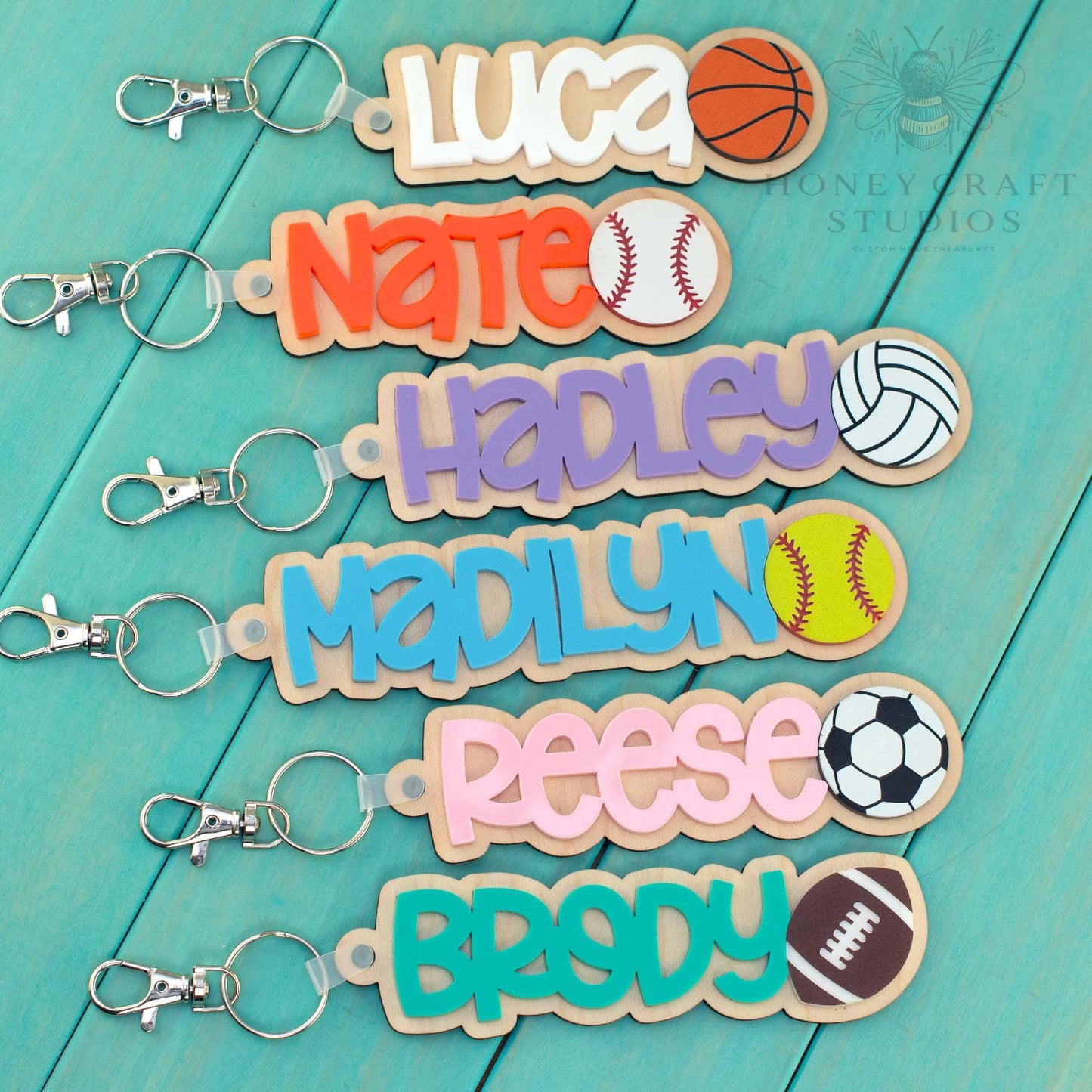 Set of personalized sports keychains with names and different ball designs including baseball, basketball, soccer, football, and volleyball
