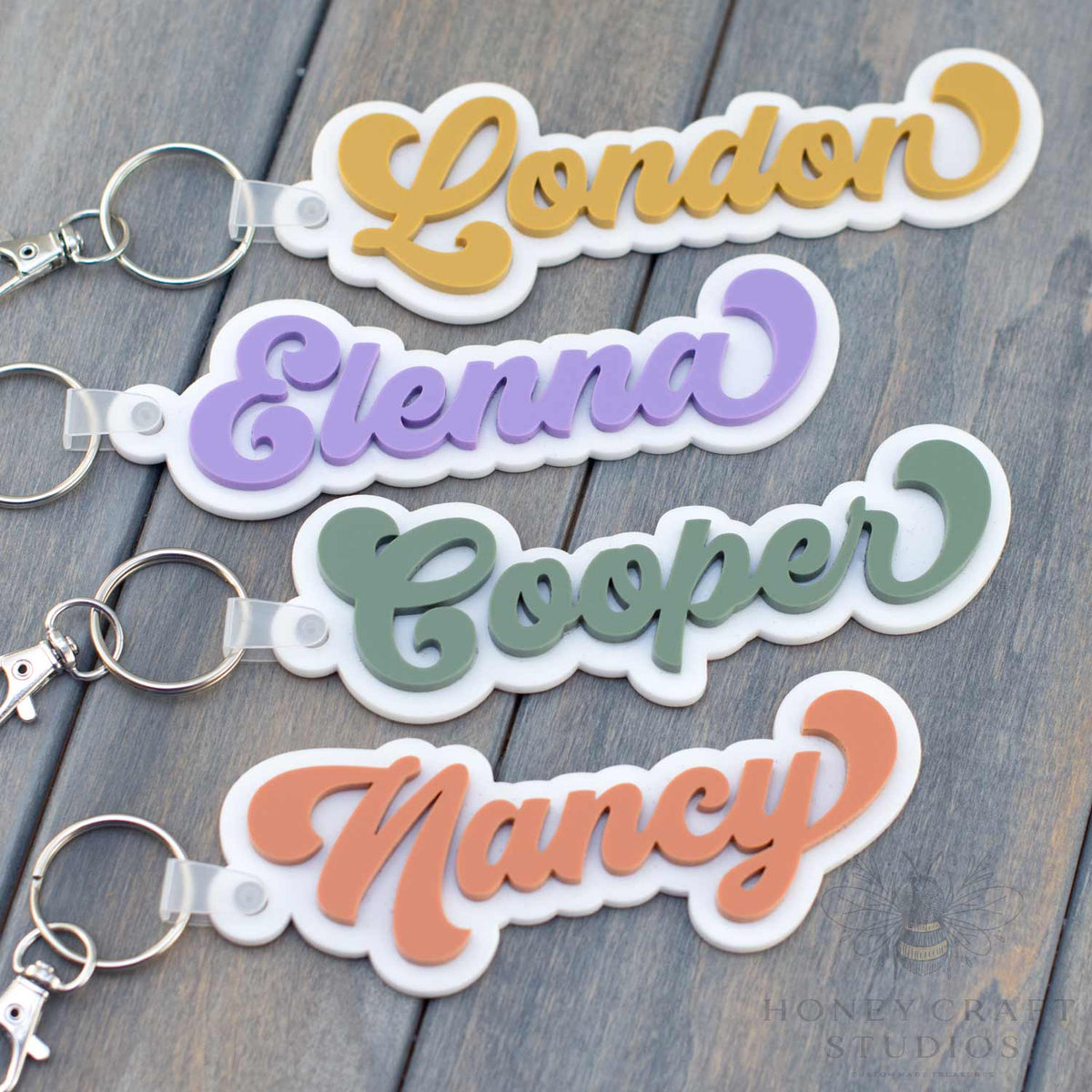 Four custom groovy-style acrylic name tags in retro colors displayed on a wooden background, showing the names London, Elenna, Cooper, and Nancy.