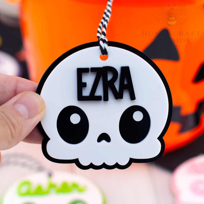 Skull-shaped name tag with 'EZRA' on a Halloween-themed background