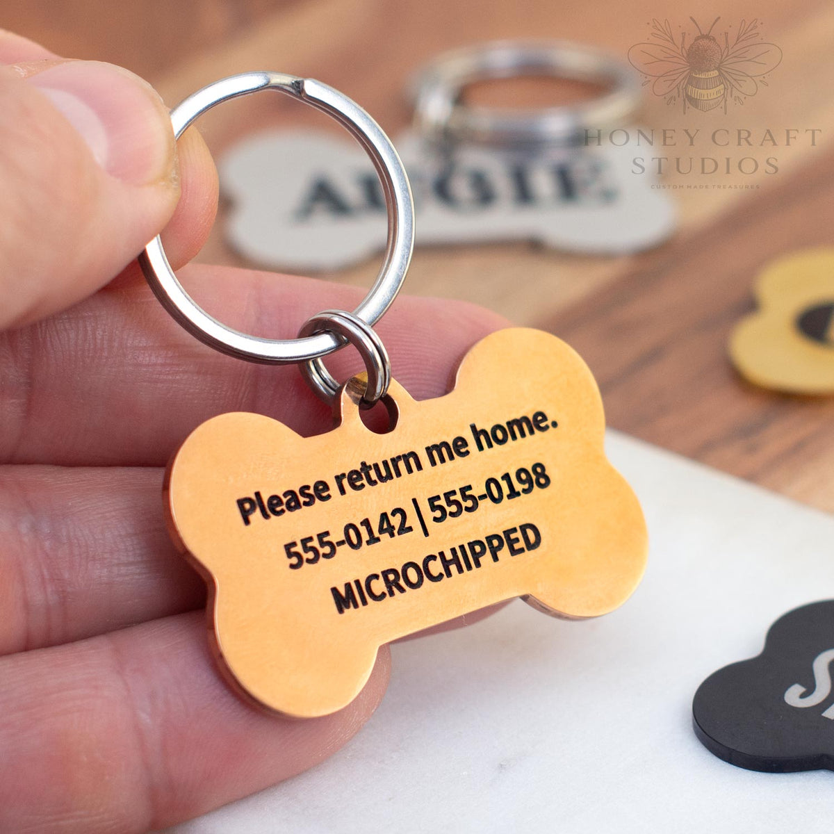 Back of custom engraved gold bone dog tag with phone numbers and “Please return me home” message