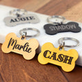 Set of personalized bone dog tags in gold, black, and silver with engraved pet names Marlie, Cash, Augie, and Shadow