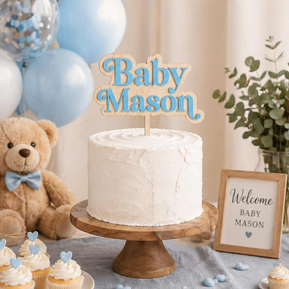 Custom baby name cake topper “Baby Mason” in blue acrylic on wood, displayed on white frosted cake with teddy bear, balloons, and baby shower decorations