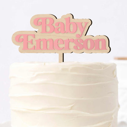 Personalized baby name cake topper with pink acrylic lettering on a wooden base, displayed on a white frosted cake for a baby shower.