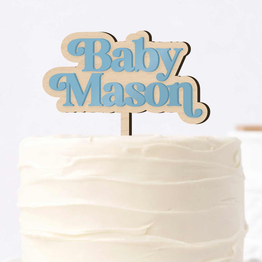 Custom baby name cake topper featuring blue acrylic lettering on a natural wooden base, shown on a white buttercream cake for a baby shower