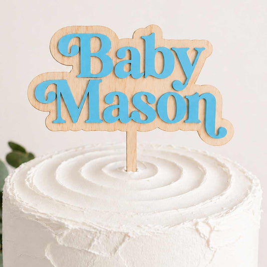 Custom baby name cake topper featuring blue acrylic lettering on a natural wooden base, shown on a white buttercream cake for a baby shower