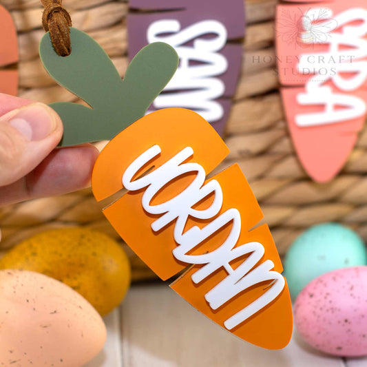 Close-up of a personalized acrylic carrot Easter basket tag held in hand, showing layered acrylic and raised name detail