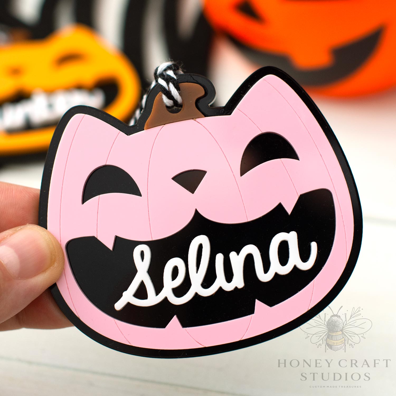 Pink and black Halloween-themed cat lack-o-lantern  keychain with 'Selina' on a blurred background