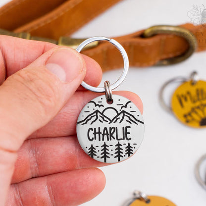 Personalized stainless steel pet ID tag with mountain and pine tree engraving and custom name Charlie in a silver finish, deep engraved pet tag.