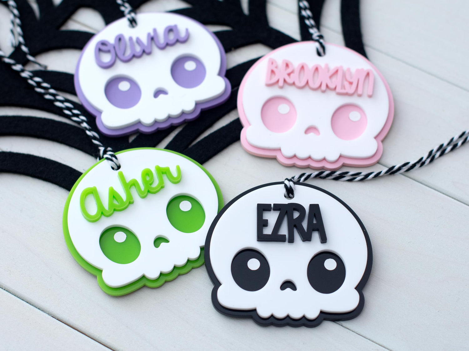 Four personalized skull-shaped name tags on necklaces with names 'Olivia', 'Brooklyn', 'Asher', and 'Ezra'.