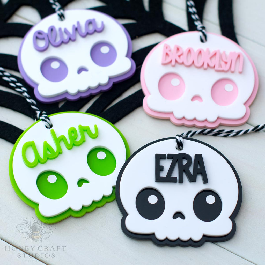 Four colorful skull-shaped name tags with names 'Olivia', 'Brooklyn', 'Asher', and 'Ezra' on a white background.