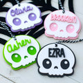 Four colorful skull-shaped name tags with names 'Olivia', 'Brooklyn', 'Asher', and 'Ezra' on a white background.