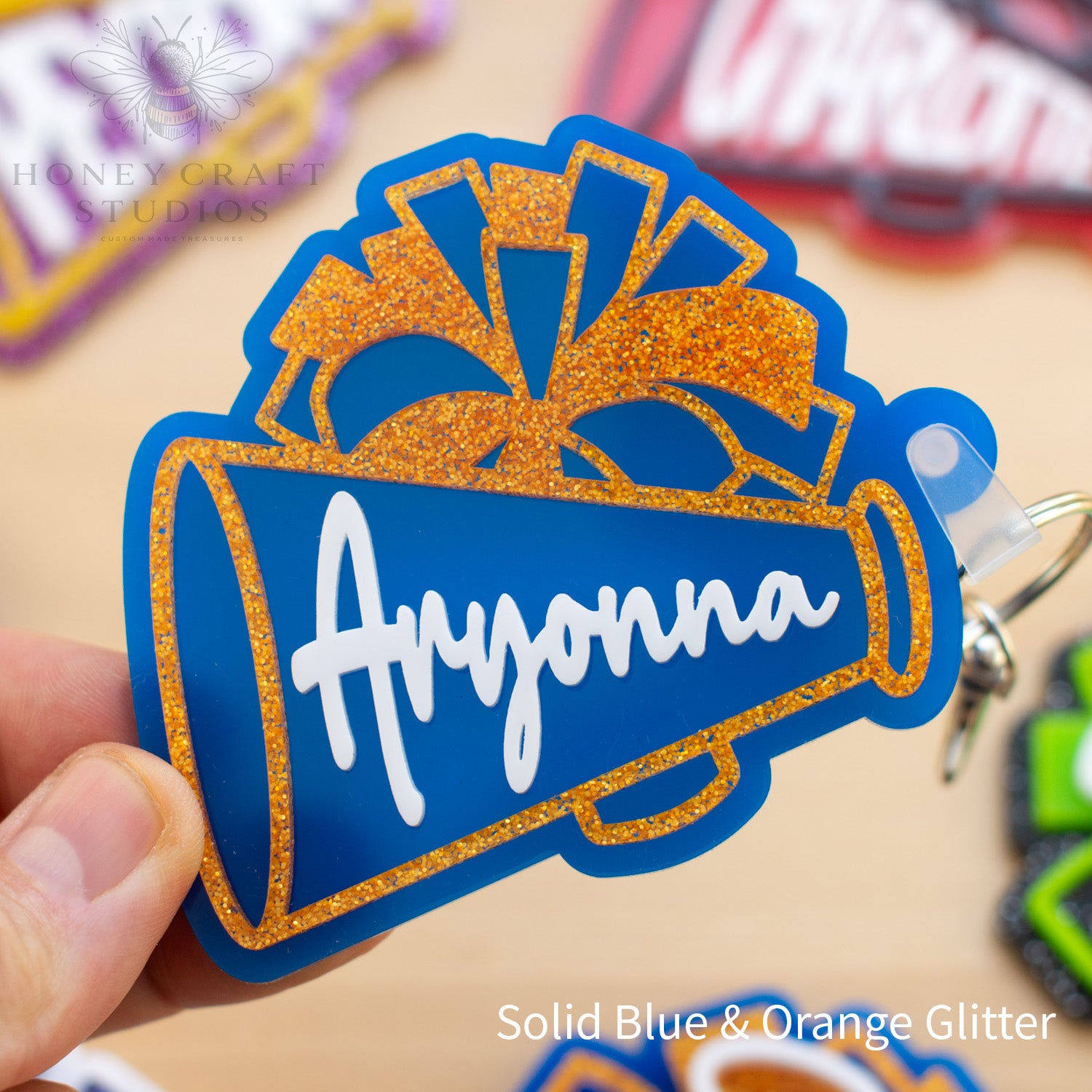 Blue and gold personalized cheer megaphone keychain featuring a custom name and glitter pom-pom design.