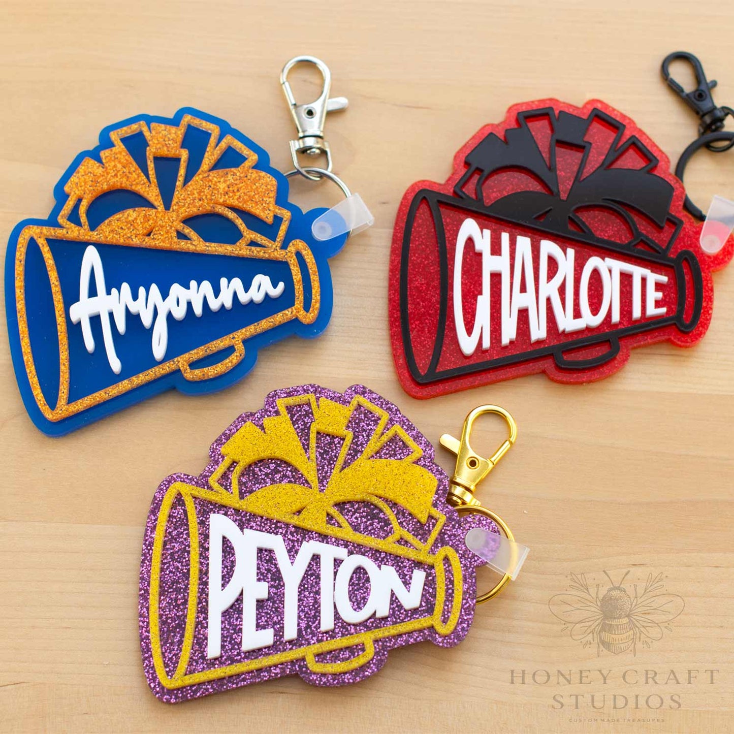 Collection of personalized cheer megaphone keychains in multiple color combinations with custom names and glitter acrylic accents.