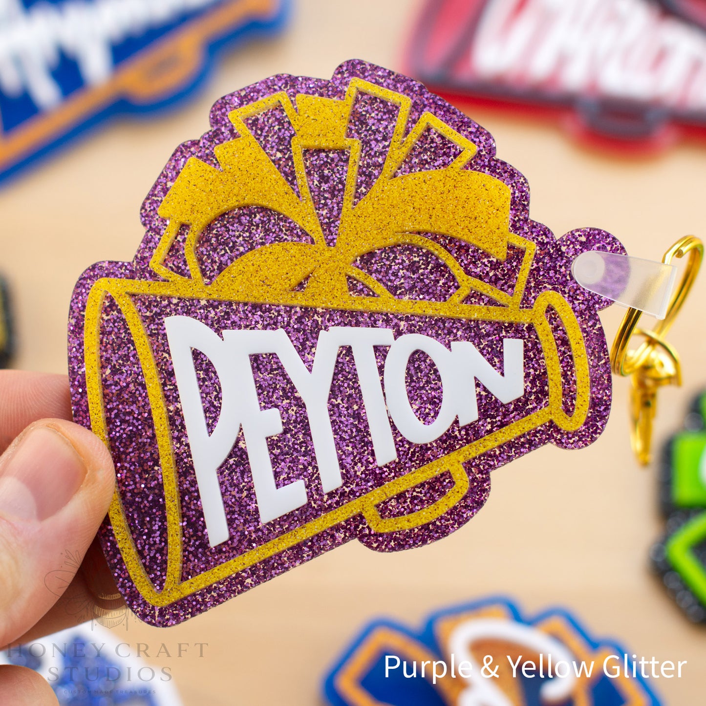 Purple and gold glitter cheer pom-pom keychain customized with a name for cheer bags and team gifts.