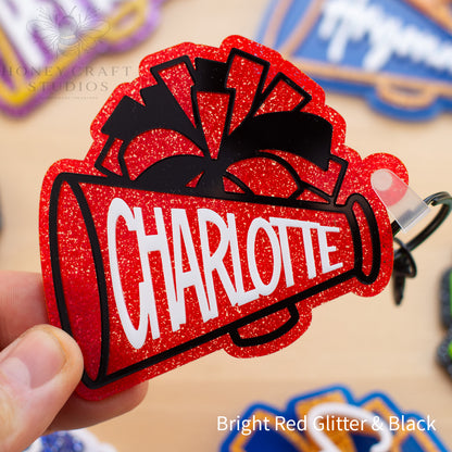 Red glitter cheerleader megaphone bag tag personalized with a custom name and layered acrylic details.
