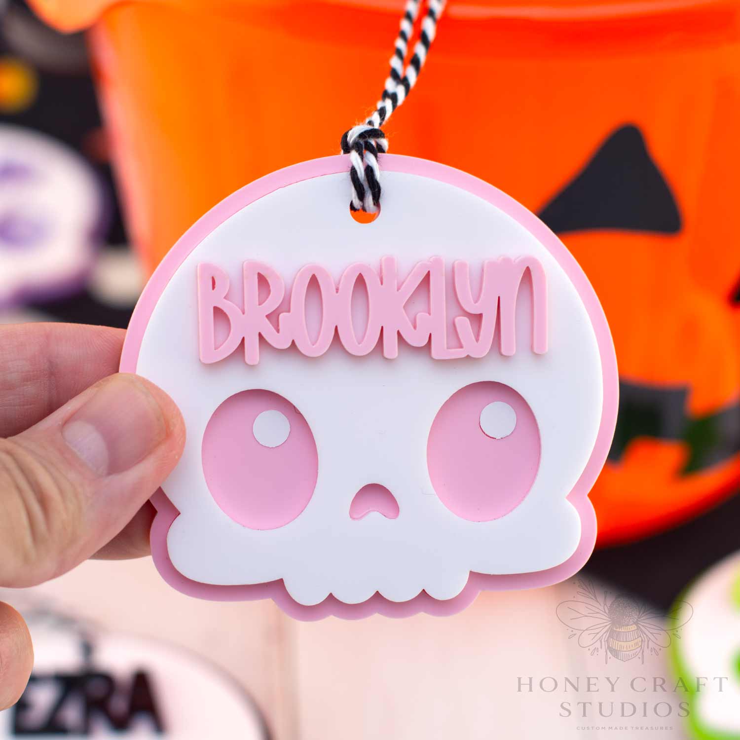 Pink skull-shaped keychain with 'Brooklyn' text held in front of a Halloween-themed background.