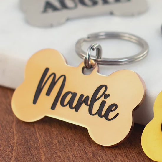 Personalized bone dog tags in gold, black, and silver with engraved pet names Marlie, Cash, Augie, and Shadow