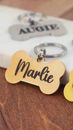 Personalized bone dog tags in gold, black, and silver with engraved pet names Marlie, Cash, Augie, and Shadow