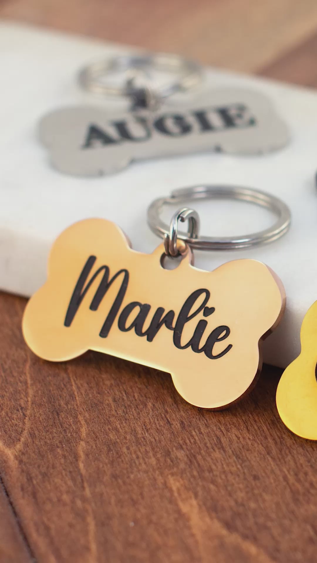 Personalized bone dog tags in gold, black, and silver with engraved pet names Marlie, Cash, Augie, and Shadow