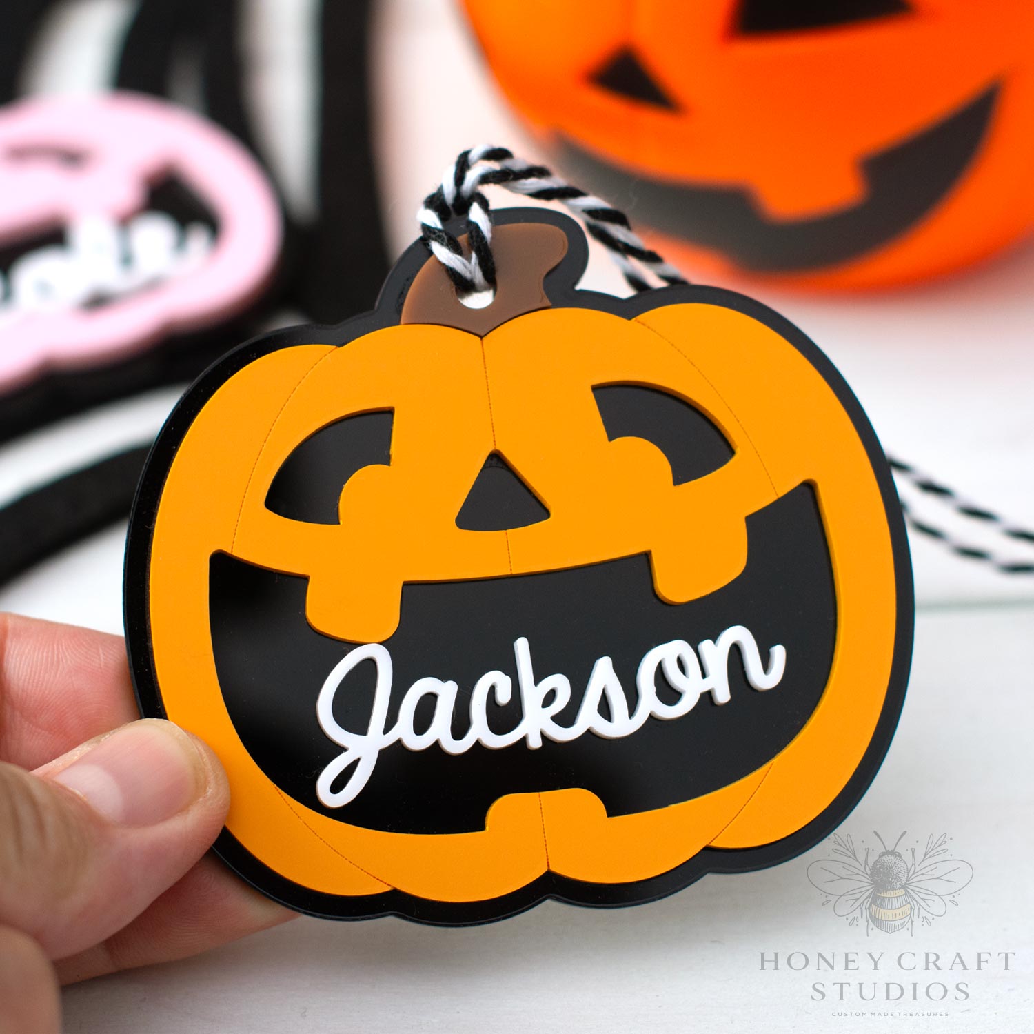 Halloween-themed pumpkin-shaped tag with 'Jackson' text, held by a hand.