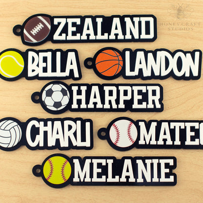 Assorted personalized sports name tags with names and different ball icons including football, basketball, tennis, soccer, volleyball, and baseball.