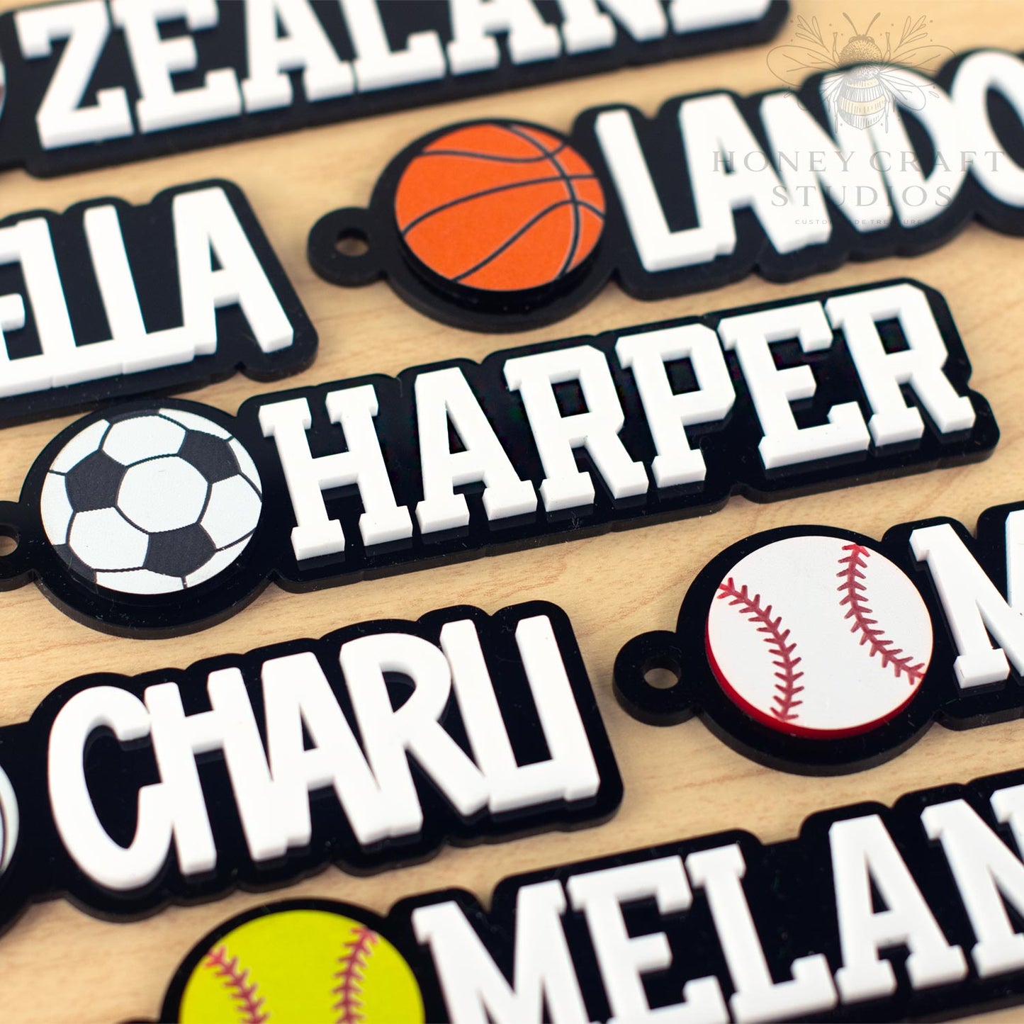 Close-up view of personalized sports name tags for backpacks showing various ball icons and names in a bold font.
