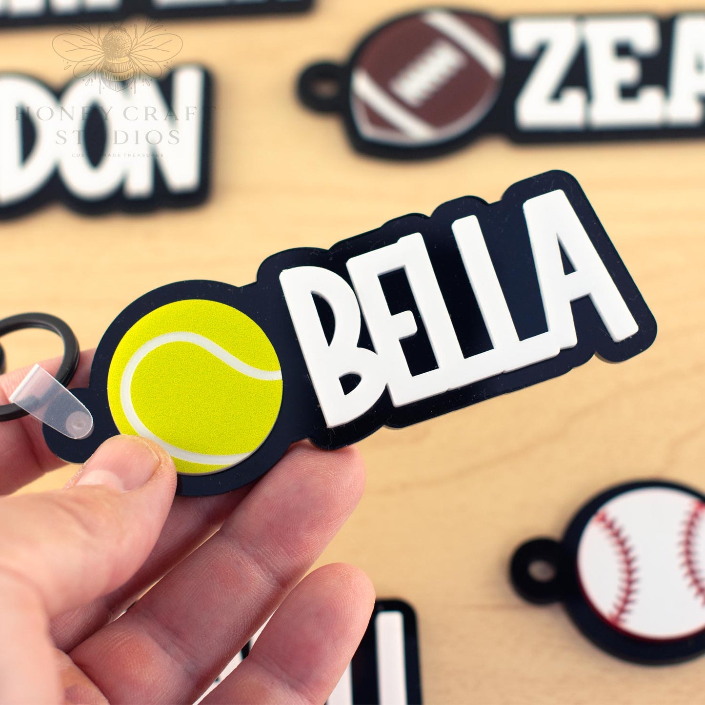 Close-up of custom tennis name tag for kids with the name “BELLA” in bold letters next to a bright yellow tennis ball.