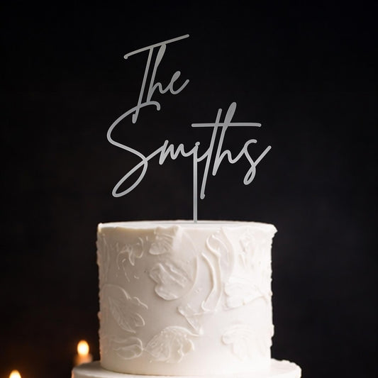 Silver mirror acrylic script wedding cake topper reading “The Smiths” on white wedding cake with embossed detailing. Made by Honey Craft Studios.
